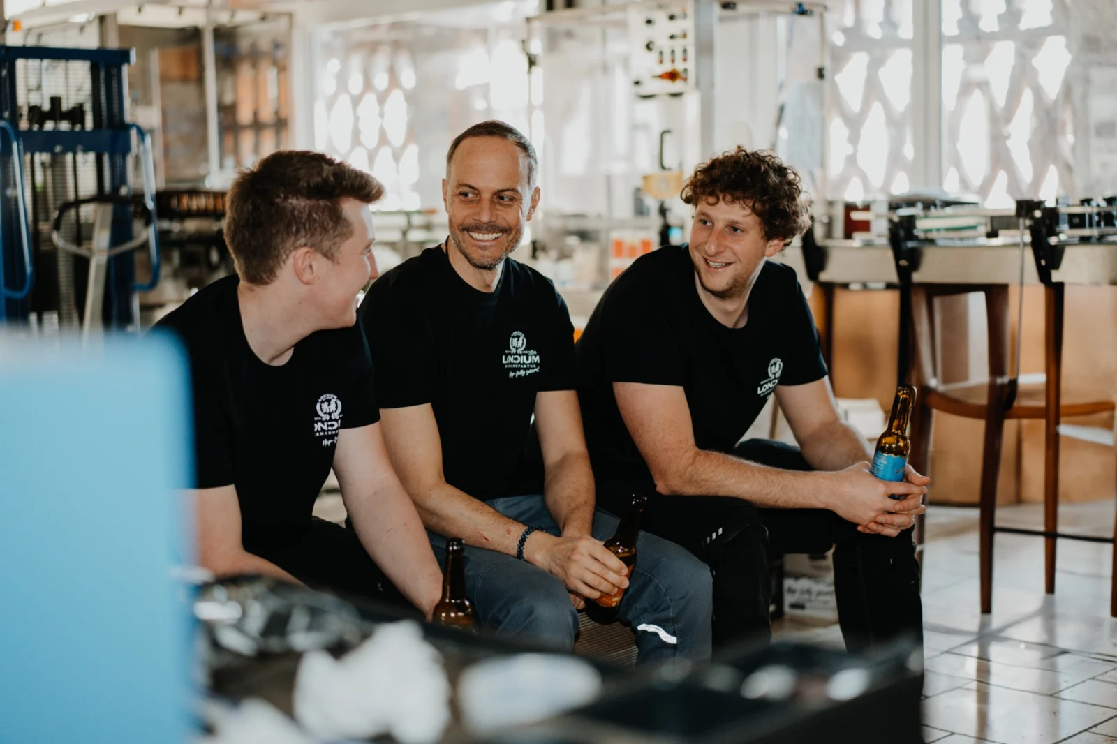 Drei Menschen aus der LONCIUM Brauerei sitzen gemeinsam zwischen den Tanks