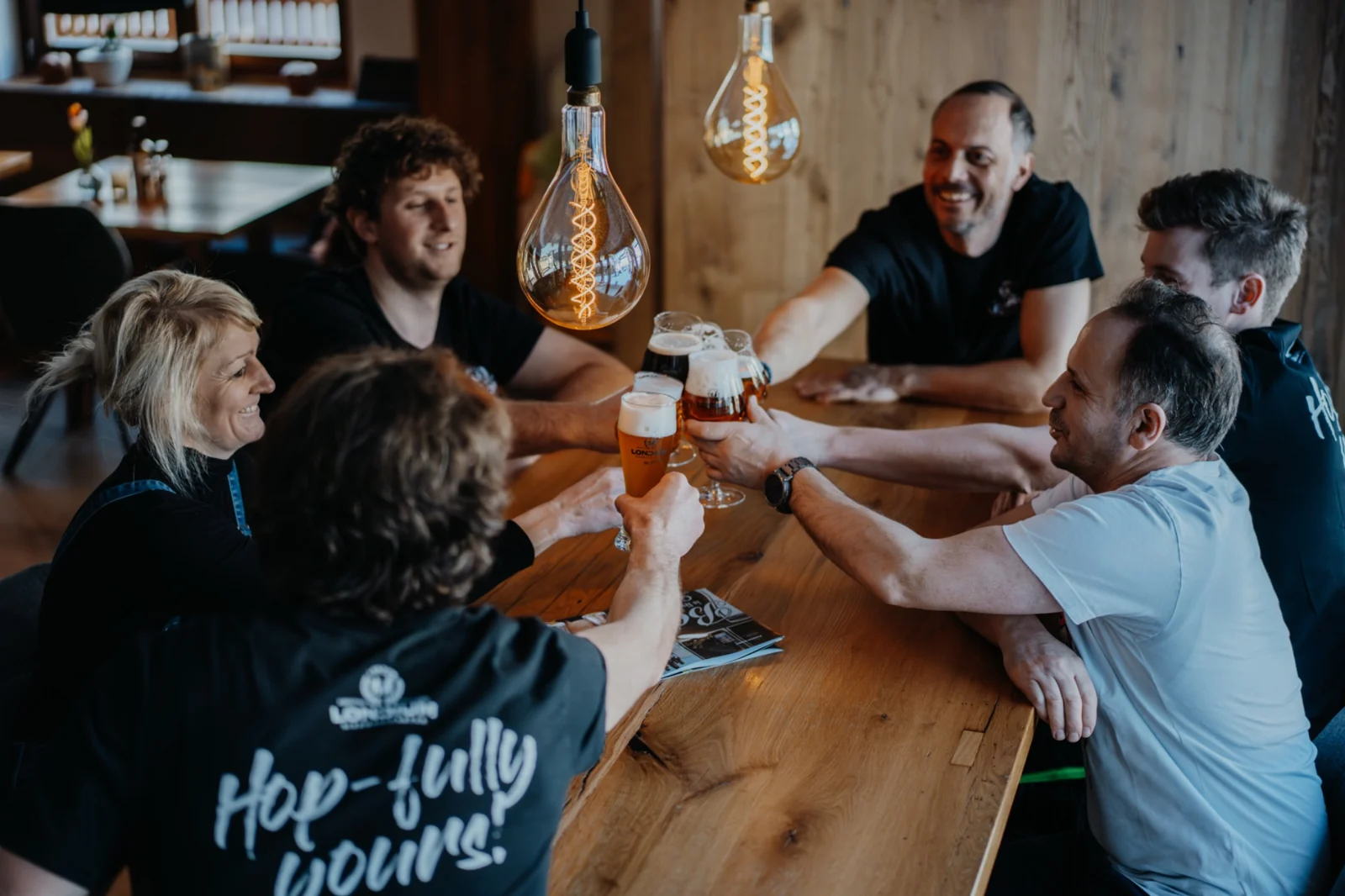 Gemeinsames Anstoßen mit LONCIUM Bieren am Holztisch im Brew Pub